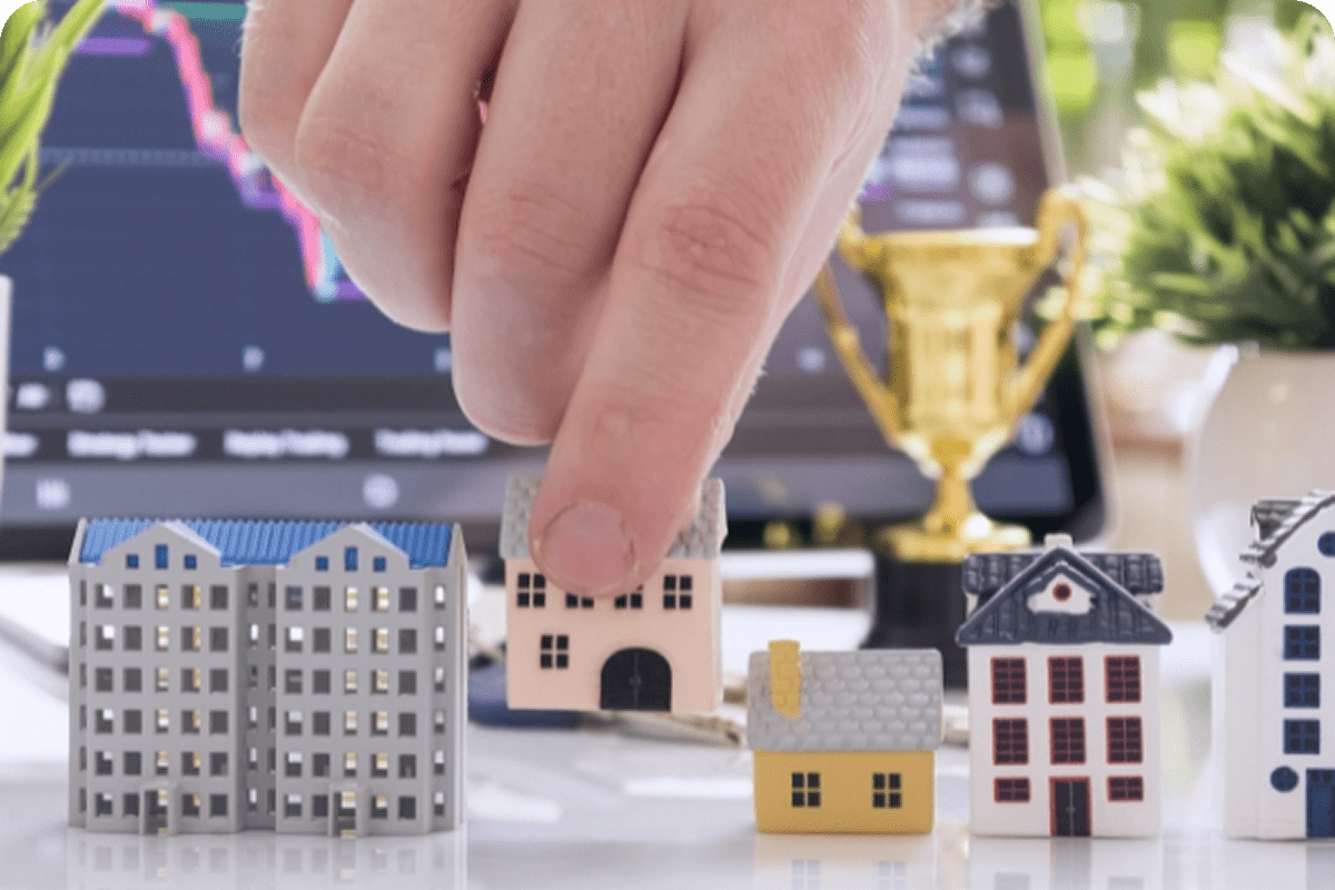 Person holding a model house over financial charts